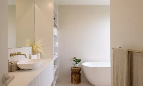Modern bathroom with a white freestanding bathtub, beige walls, a floating sink vanity with brass faucet