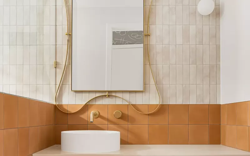 A modern bathroom with a gold-framed mirror, and white and brown tiles