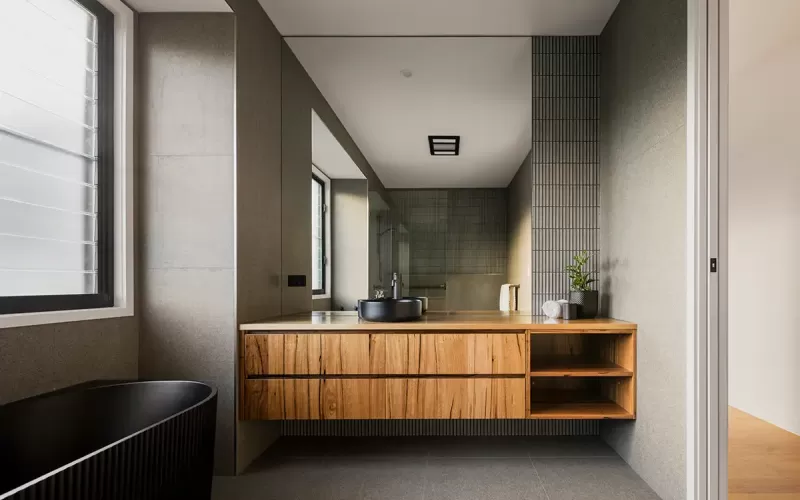 A modern bathroom with a wooden vanity, a natural stone basin, and a round mirror with backlighting