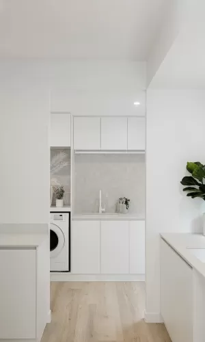 A minimalist laundry room with white cabinets, a washing machine, and a plant on the counter
