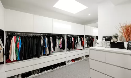 Spacious and modern walk-in closet with white cabinets, drawers, and shelves filled with clothes and shoes