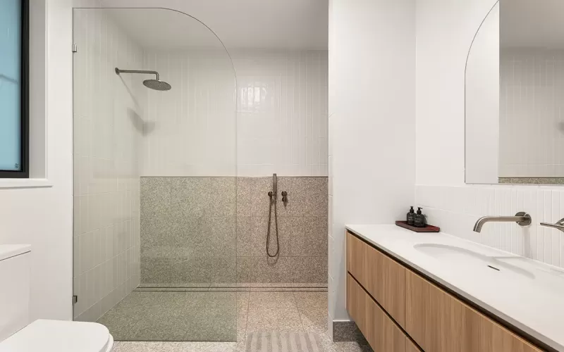 Modern bathroom interior with a walk-in shower, white tiles on the walls, and terrazzo tiles on the floor and lower half of the shower area