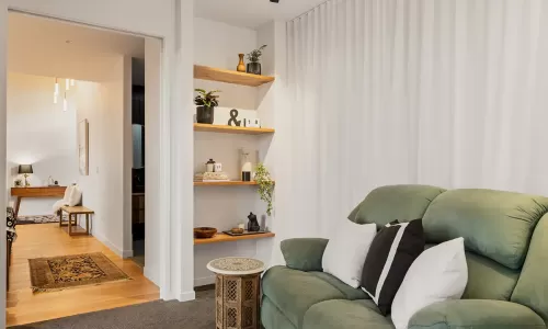 A cozy living room with a green couch, wooden side table and floating wooden shelves on the wall