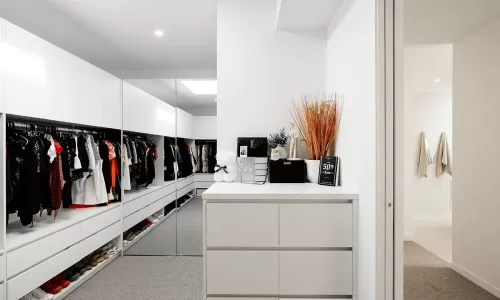 A modern, well-organized walk-in closet with white built-in cabinets and large mirrors