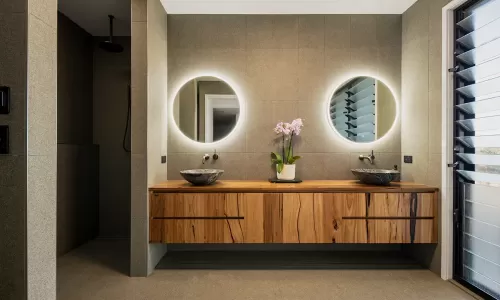 A modern bathroom with a wooden vanity and two round mirrors with backlighting