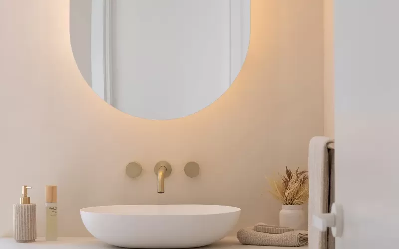 Bathroom vanity wall with a round mirror, white oval sink, and gold fixtures
