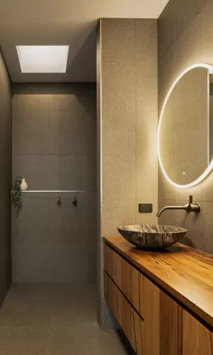 A modern bathroom with grey tiled walls, and a large round mirror with LED lighting