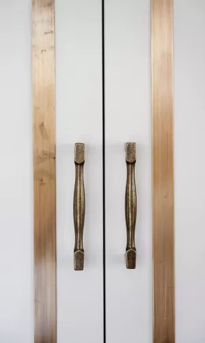 Close-up of white cabinet doors with brass trim and antique-style brass handles in a modern kitchen