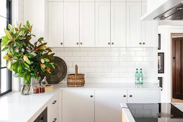 A bright kitchen with white cabinetry, wood floors, a yellow island, and greenery by the window