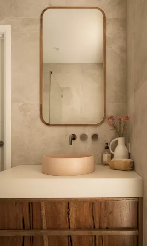 Modern bathroom with wooden vanity, beige round sink, large mirror, and decorative flowers in a vase