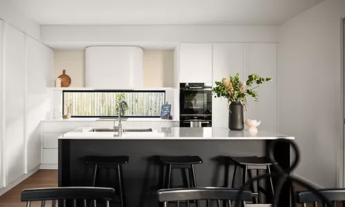 Modern kitchen with a large white island, black barstools, white cabinetry, an integrated oven, and a decorative plant arrangement on the counter