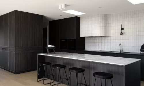 Modern kitchen with dark wood cabinets, a marble island, black stools, and a white tiled backsplash