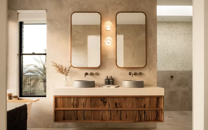 Modern bathroom with double sinks, wooden vanity, dual mirrors, wall lights, and a window with a view