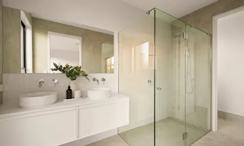 Modern bathroom with dual sinks, large mirror, glass-enclosed shower, and a vase with greenery on the counter