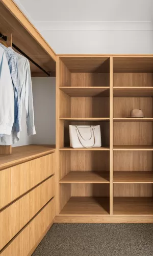 Walk-in closet with wooden shelves, hanging shirts, a white handbag, and a hat on the shelves