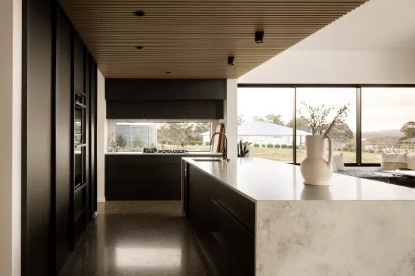 Modern kitchen with black cabinets, marble island, wooden ceiling, and large windows with scenic views