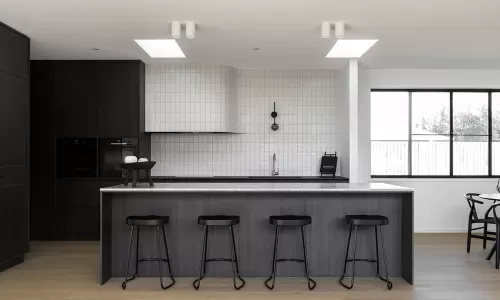 Contemporary kitchen with dark wood cabinets, a marble island, black stools, and white tiled walls