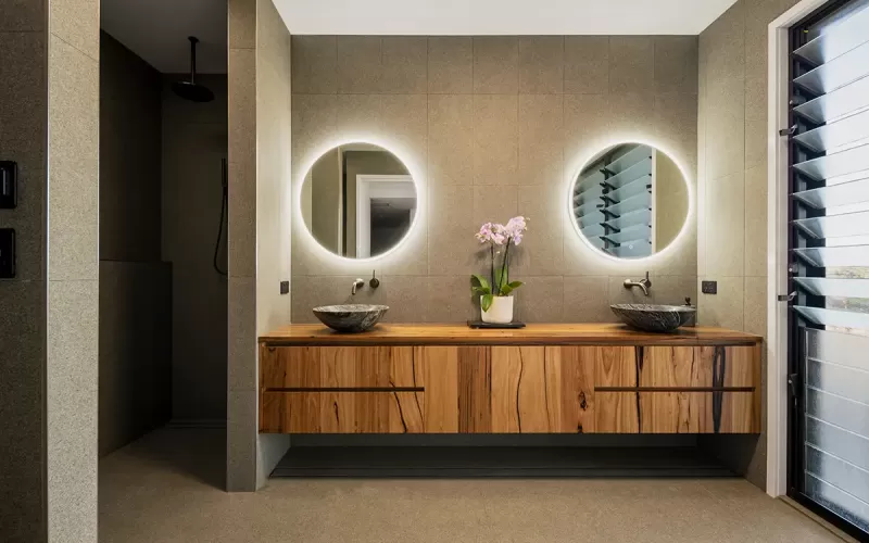 Modern bathroom with black tiled walls, round mirror, wooden vanity with black basin