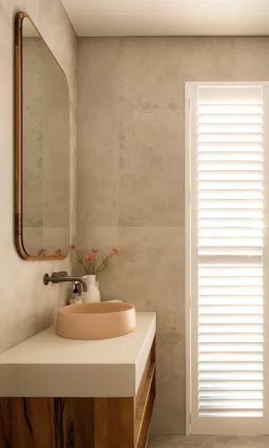 Modern bathroom with wooden vanity, round beige sink, large mirror, and shuttered window for natural light