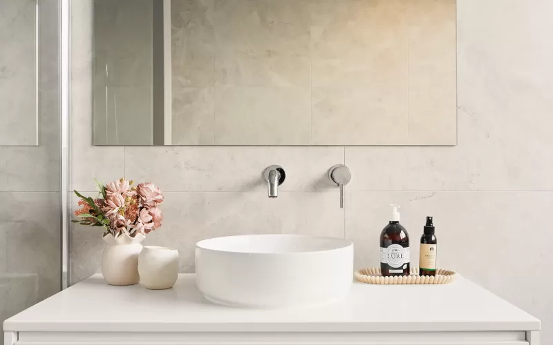 Modern bathroom with a round sink, large mirror, flowers in a vase, and toiletries on the counter