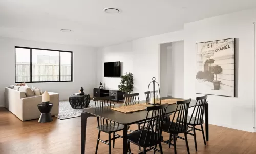 Open living and dining area with black chairs, a beige sofa, a Chanel print, and a large window