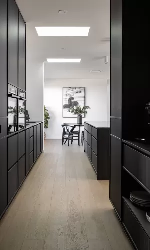 Sleek kitchen with black cabinetry, light wood flooring, skylights, and a modern dining area in view