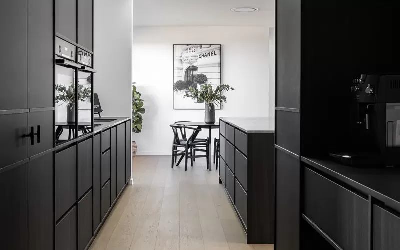 Modern kitchen with sleek black cabinets, light wood flooring, skylights, and a small dining area in the back