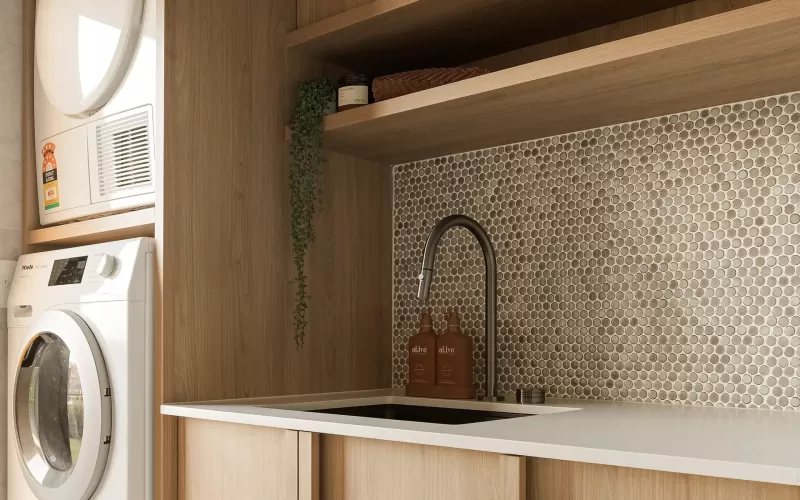 Modern laundry room with wooden cabinets, stacked washer and dryer, penny tile backsplash, and sink