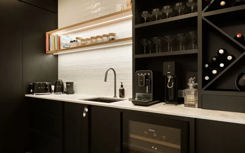 Modern kitchen with black cabinets, Smeg appliances, white tile backsplash, wine storage, and shelves