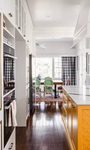 Kitchen with yellow island, marble countertop, and view into dining area with green chairs and windows