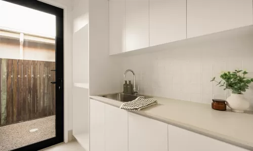 Modern laundry room with a stainless steel sink, white cabinets, countertop decor, and a glass door