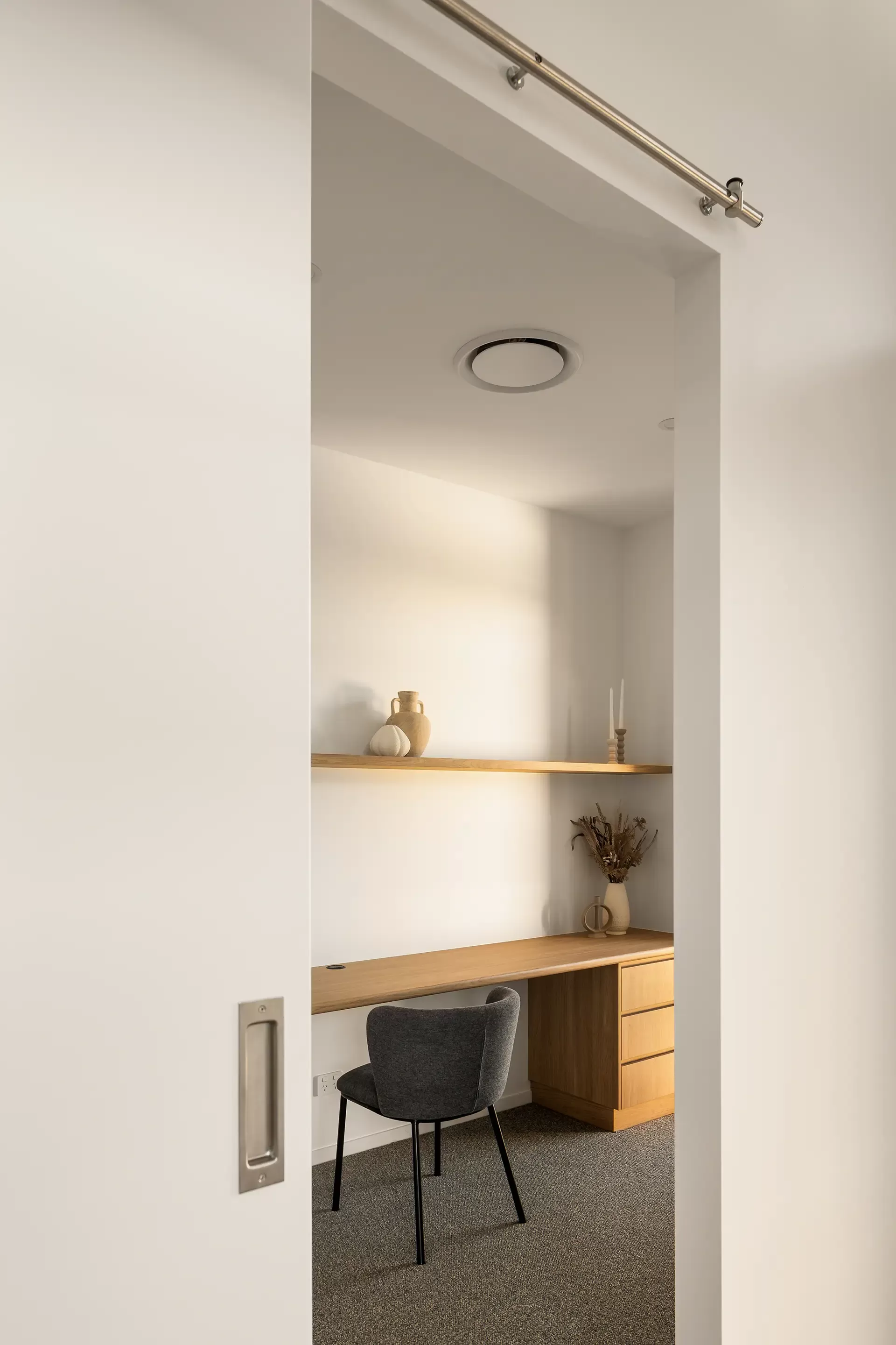 A minimalist home office with a wooden desk, a gray chair, shelves, decorative items, and a sliding door