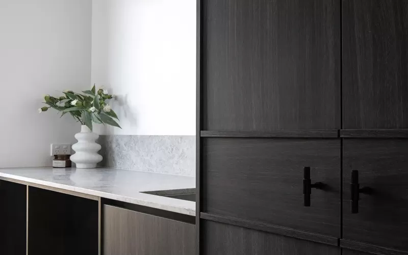 A modern bathroom vanity with a white vessel sink, gray stone countertop, white tile backsplash, and dried floral arrangement