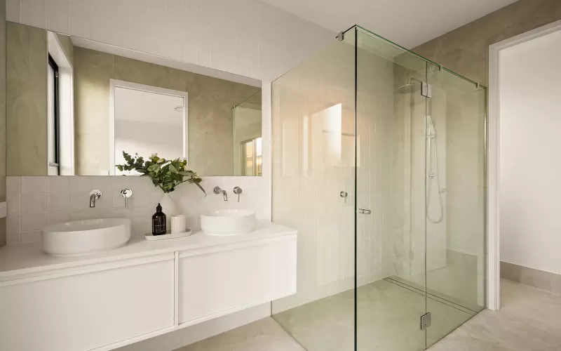 Modern bathroom with dual sinks, large mirror, glass-enclosed shower, and a vase with greenery on the counter.