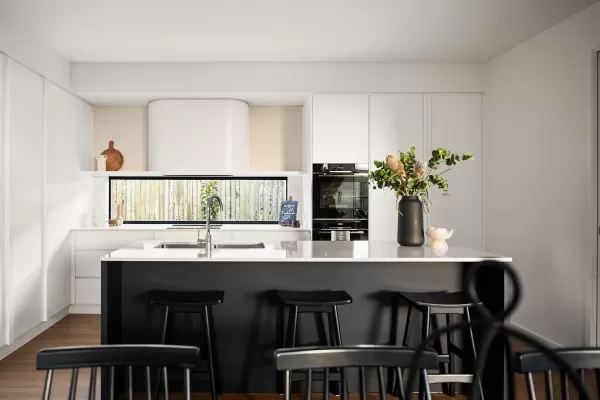 A modern kitchen with white cabinets, a black island, bar stools, and a large window behind the sink