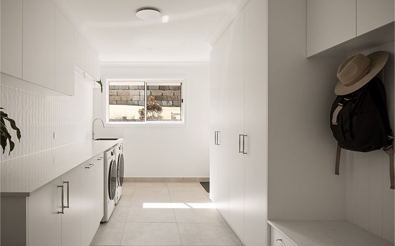 A long row of white cabinets and countertops along one wall, with a washing machine and dryer visible.