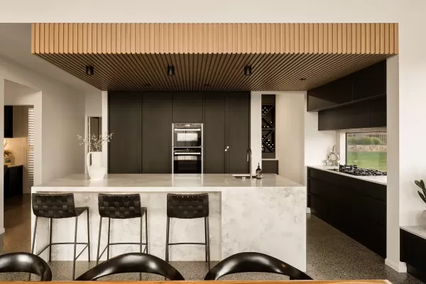 Modern kitchen with marble island, black cabinets, wooden ceiling, bar stools, and built-in appliances