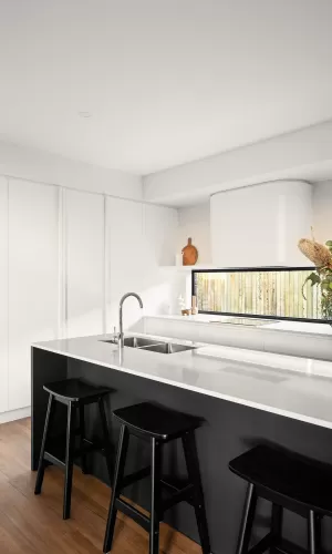 Modern kitchen with white cabinets, black stools, a white island, and a sink under a large window