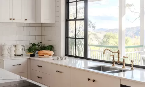 Modern kitchen with large window, white cabinets, subway tile, brass faucet, and bread on the counter