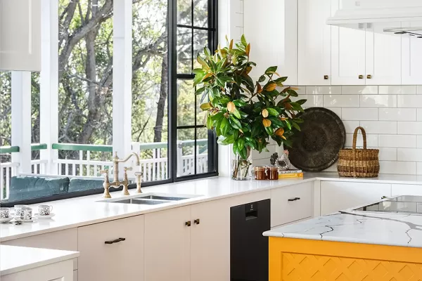 A stylish kitchen with white cabinets, large windows, and a yellow island, featuring natural light.