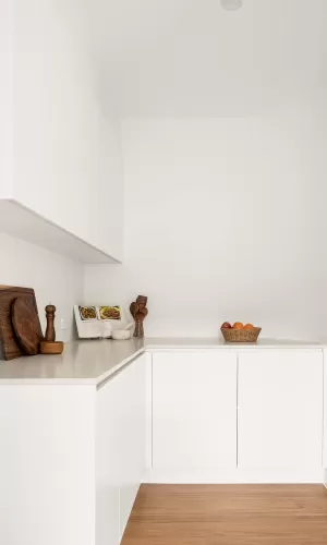 Minimalist white kitchen nook with wooden cutting boards, utensils, a cookbook, and a fruit basket