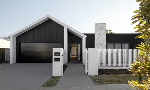 A modern home exterior with a black garage door, white fence, stone chimney, and a minimalist design