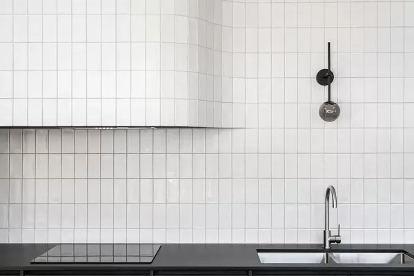 A modern kitchen with dark wood cabinets, a black countertop, a curved white tile backsplash, and a sleek faucet